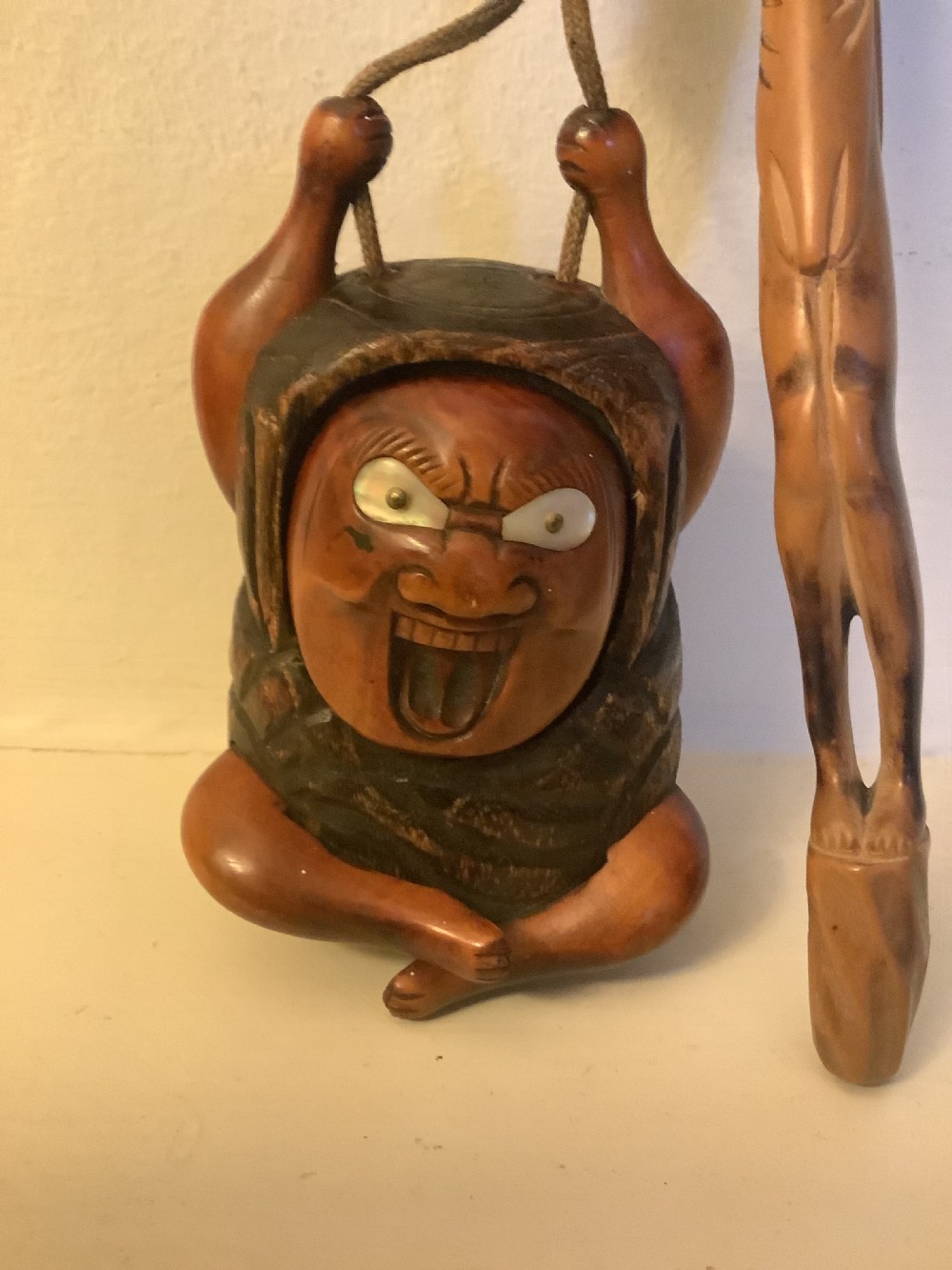 A carved wooden Japanese tobacco container featuring a wide-eyed Daruma figure connected by a cord and bead to an elongated carved wooden pipe holder. View III