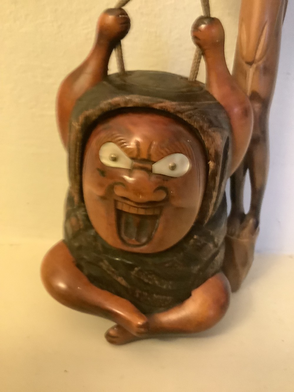 A carved wooden Japanese tobacco container featuring a wide-eyed Daruma figure connected by a cord and bead to an elongated carved wooden pipe holder. View IV