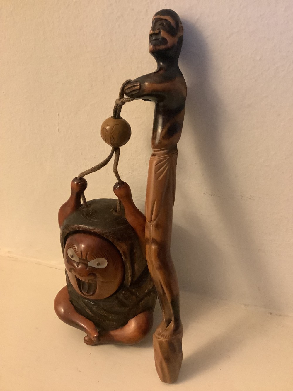 A carved wooden Japanese tobacco container featuring a wide-eyed Daruma figure connected by a cord and bead to an elongated carved wooden pipe holder. View V