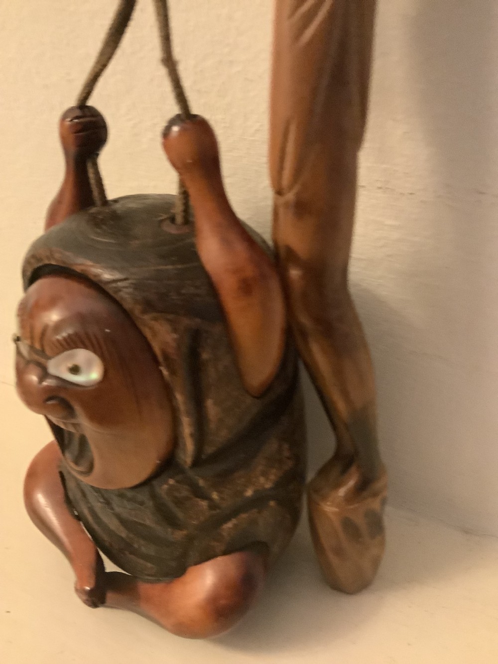 A carved wooden Japanese tobacco container featuring a wide-eyed Daruma figure connected by a cord and bead to an elongated carved wooden pipe holder. View VI