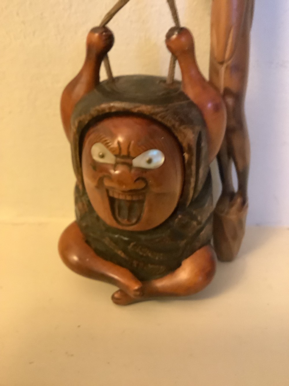 A carved wooden Japanese tobacco container featuring a wide-eyed Daruma figure connected by a cord and bead to an elongated carved wooden pipe holder. View VII