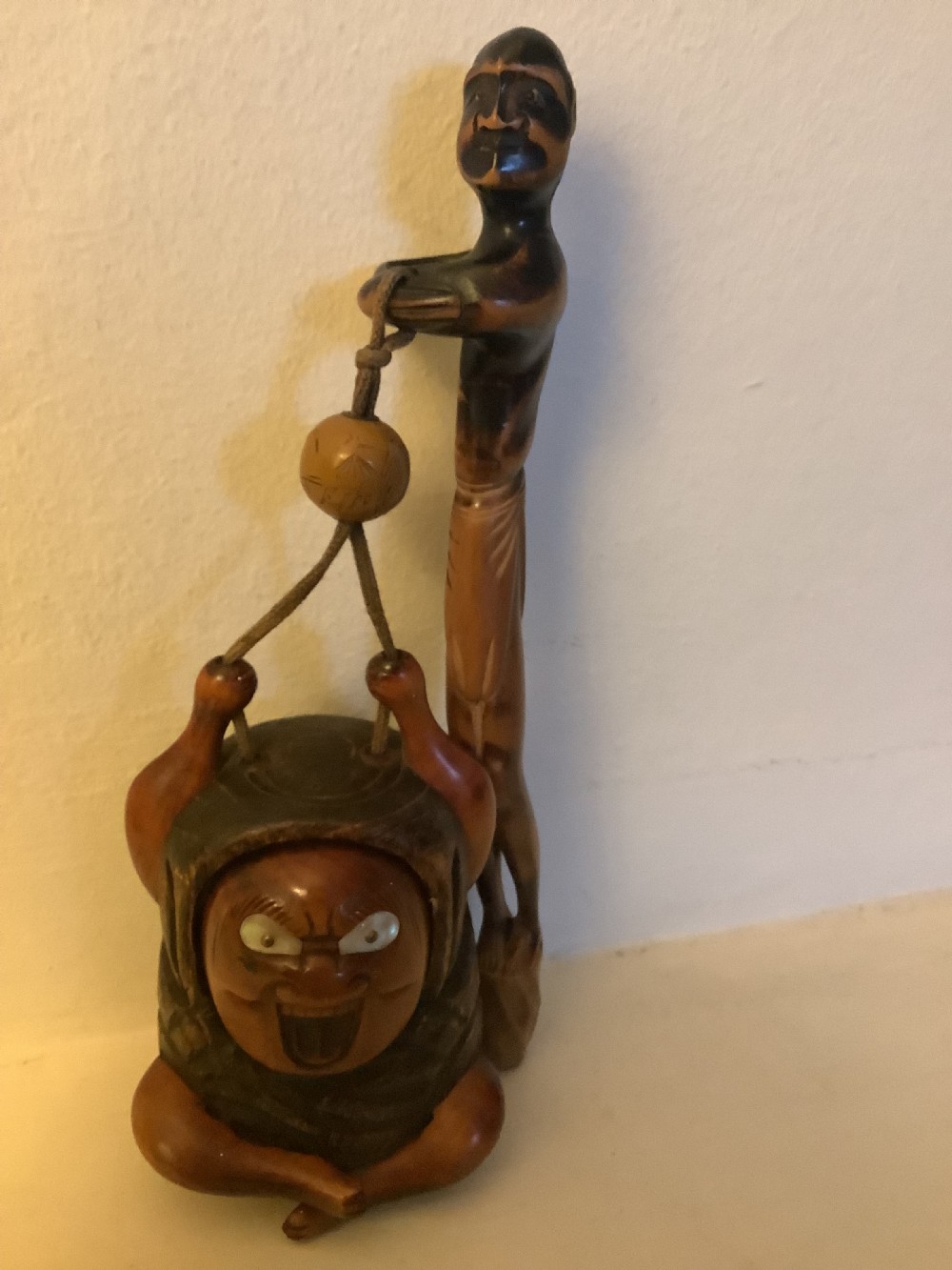 A carved wooden Japanese tobacco container featuring a wide-eyed Daruma figure connected by a cord and bead to an elongated carved wooden pipe holder. View VIII