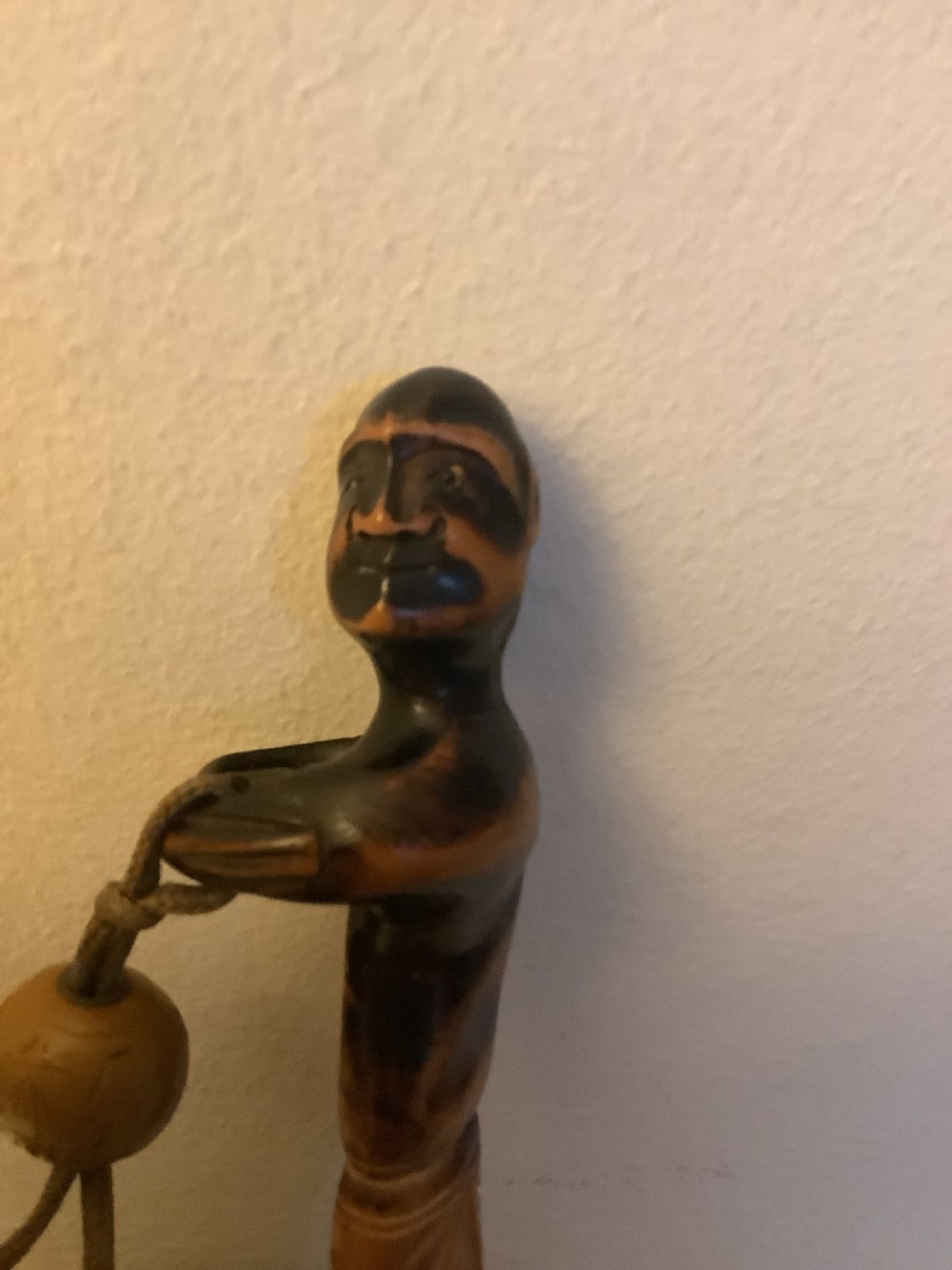 A carved wooden Japanese tobacco container featuring a wide-eyed Daruma figure connected by a cord and bead to an elongated carved wooden pipe holder. View IX