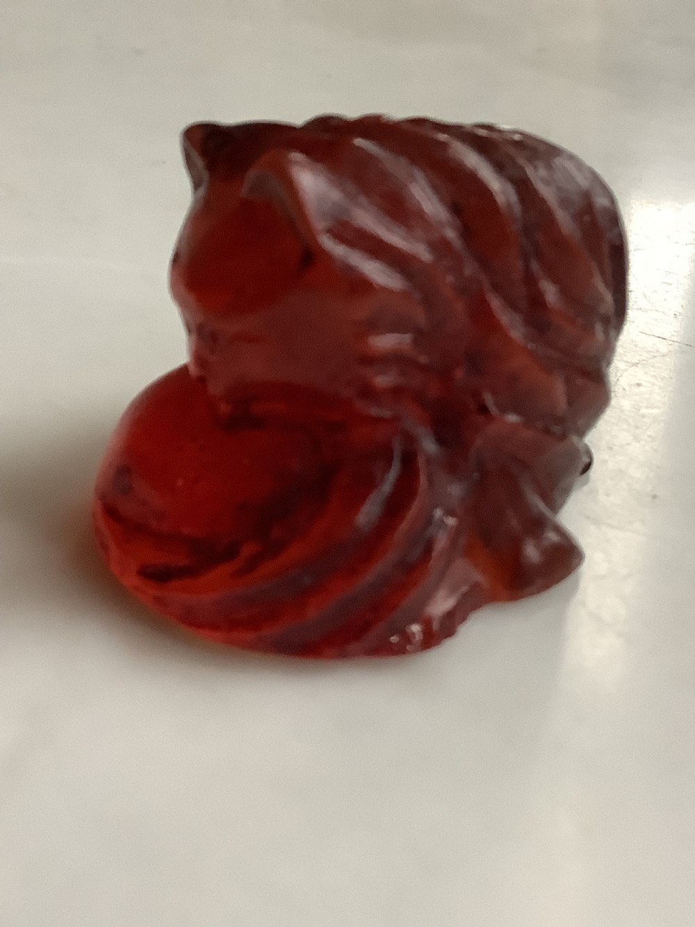 A small, translucent cherry amber carving depicting a curled sleeping cat with incised fur details. View III