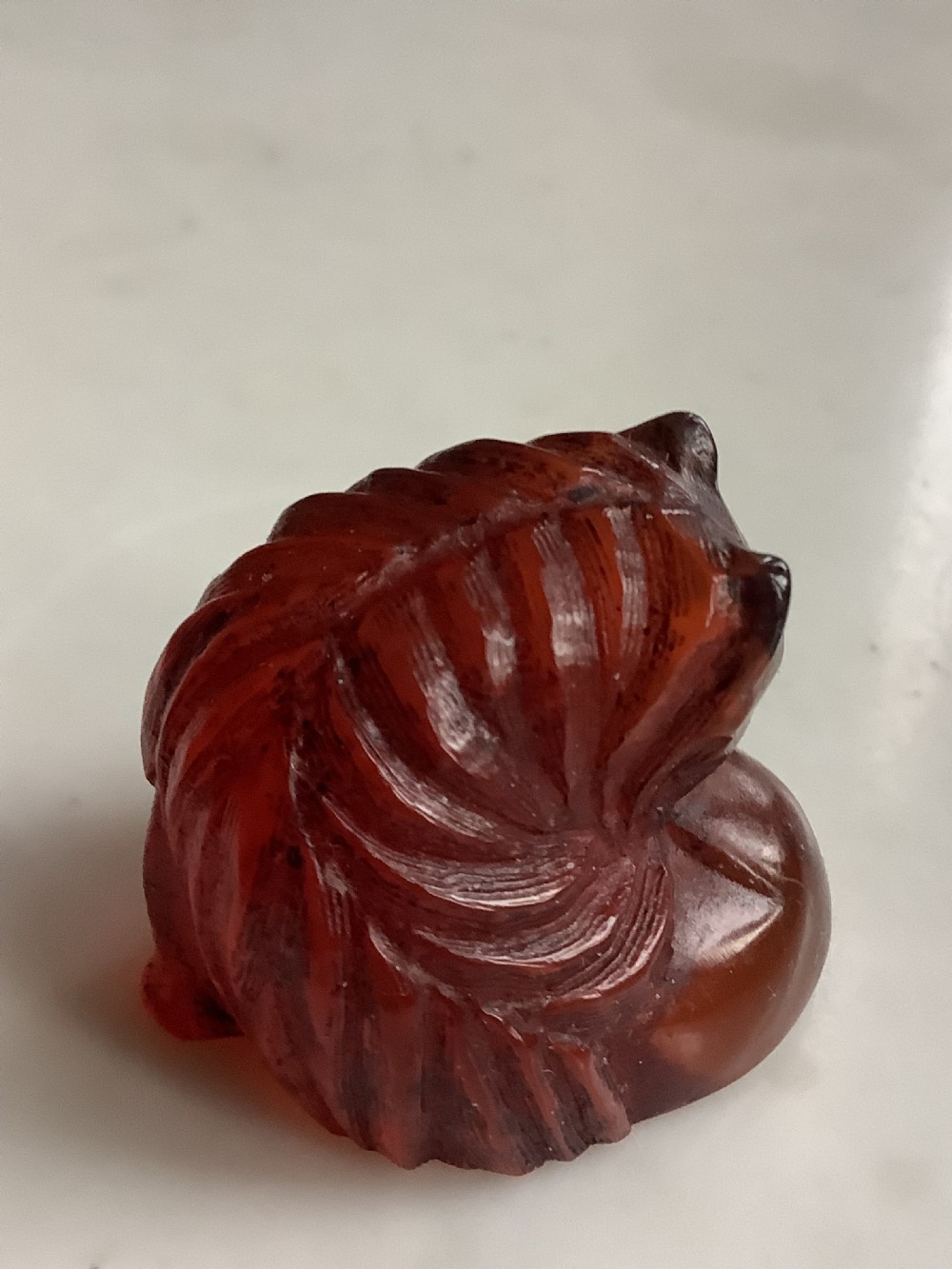 A small, translucent cherry amber carving depicting a curled sleeping cat with incised fur details. View II
