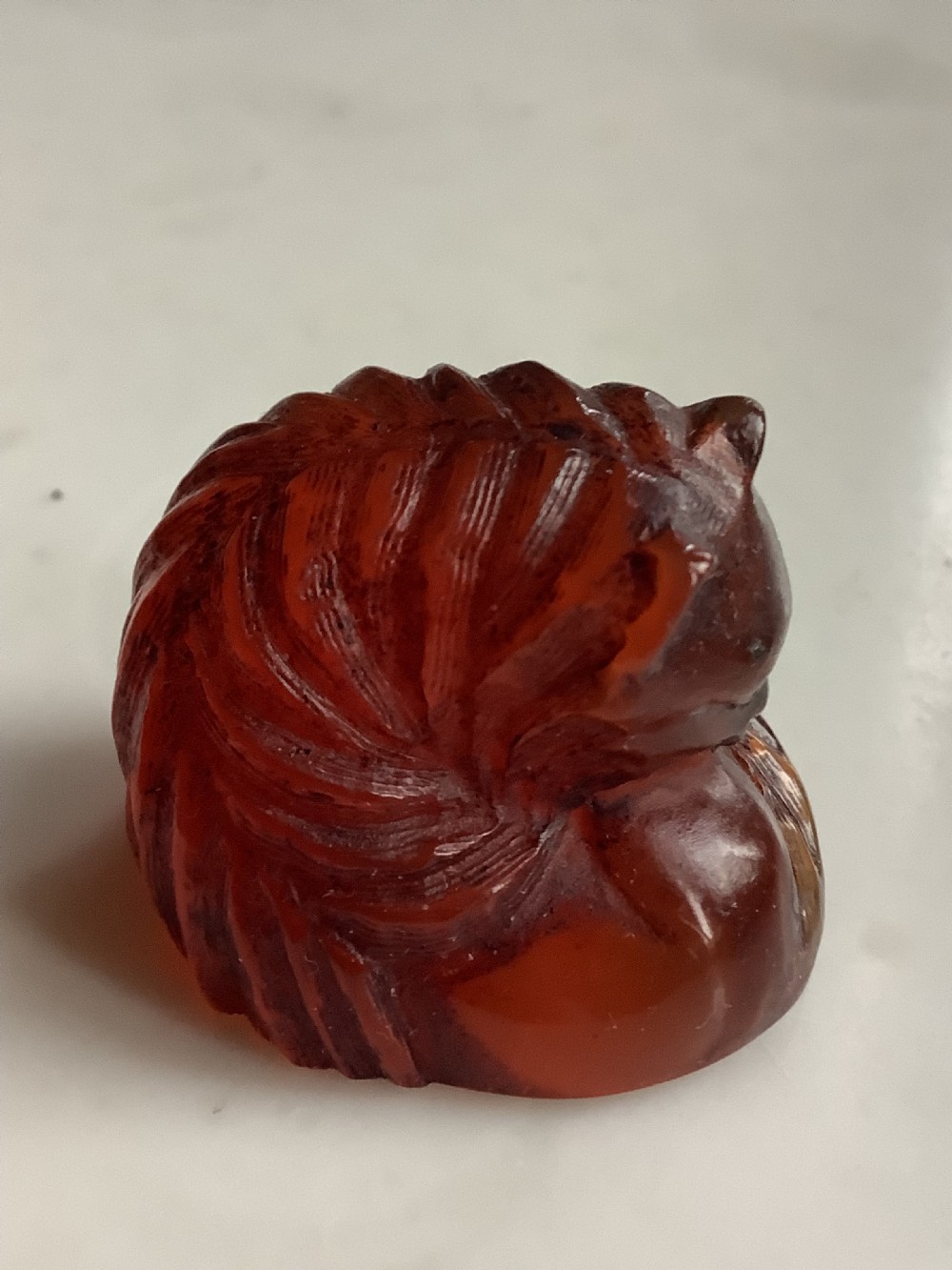 A small, translucent cherry amber carving depicting a curled sleeping cat with incised fur details.