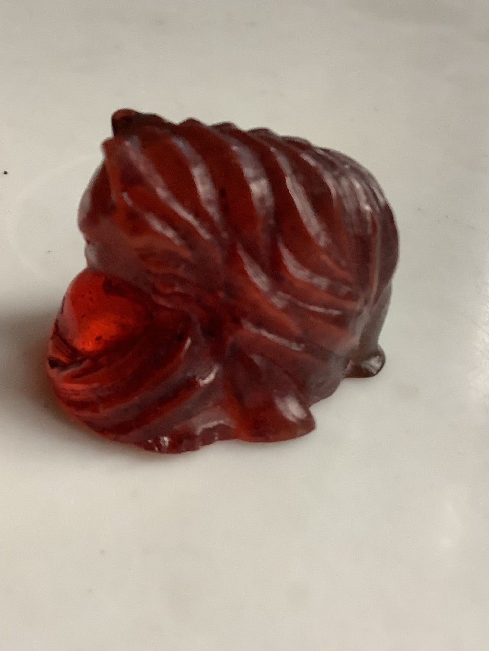 A small, translucent cherry amber carving depicting a curled sleeping cat with incised fur details. View IV