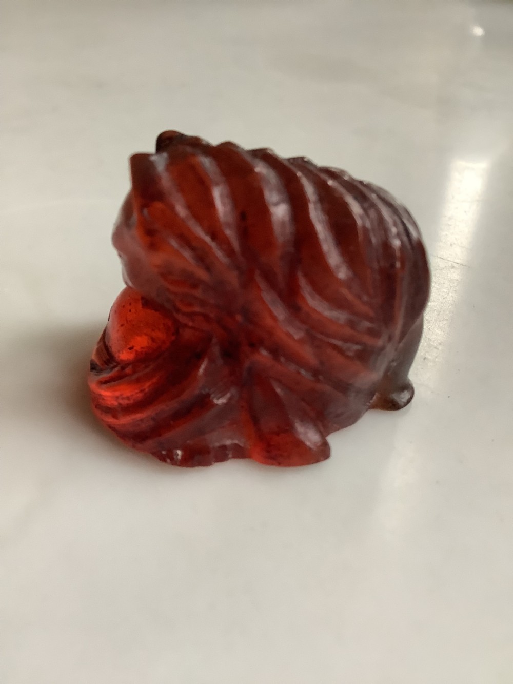 A small, translucent cherry amber carving depicting a curled sleeping cat with incised fur details. View V