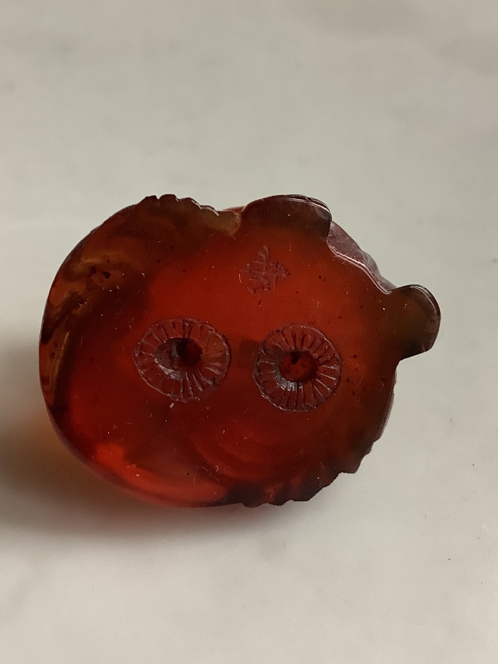 A small, translucent cherry amber carving depicting a curled sleeping cat with incised fur details. View VII