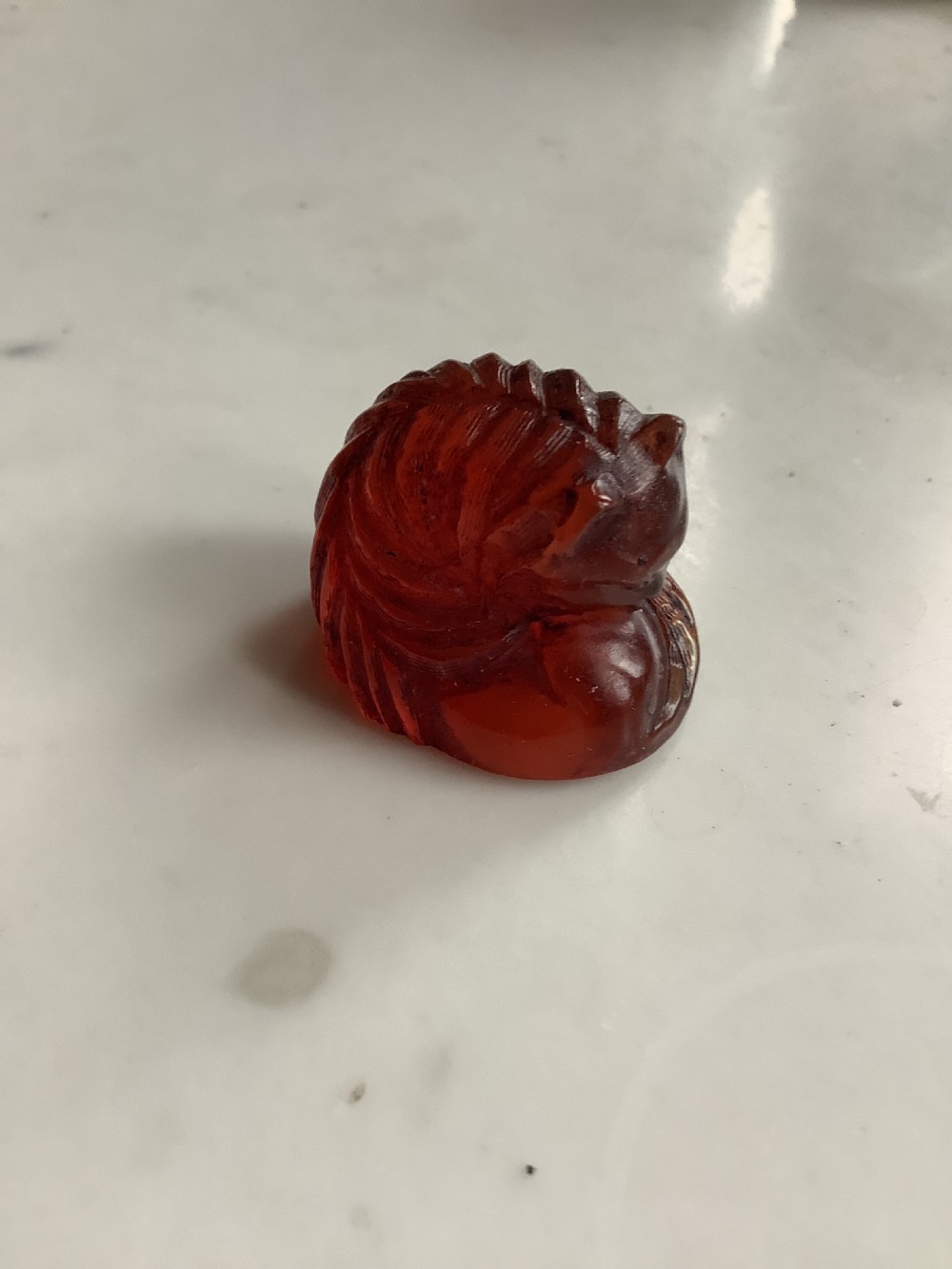 A small, translucent cherry amber carving depicting a curled sleeping cat with incised fur details. View VIII