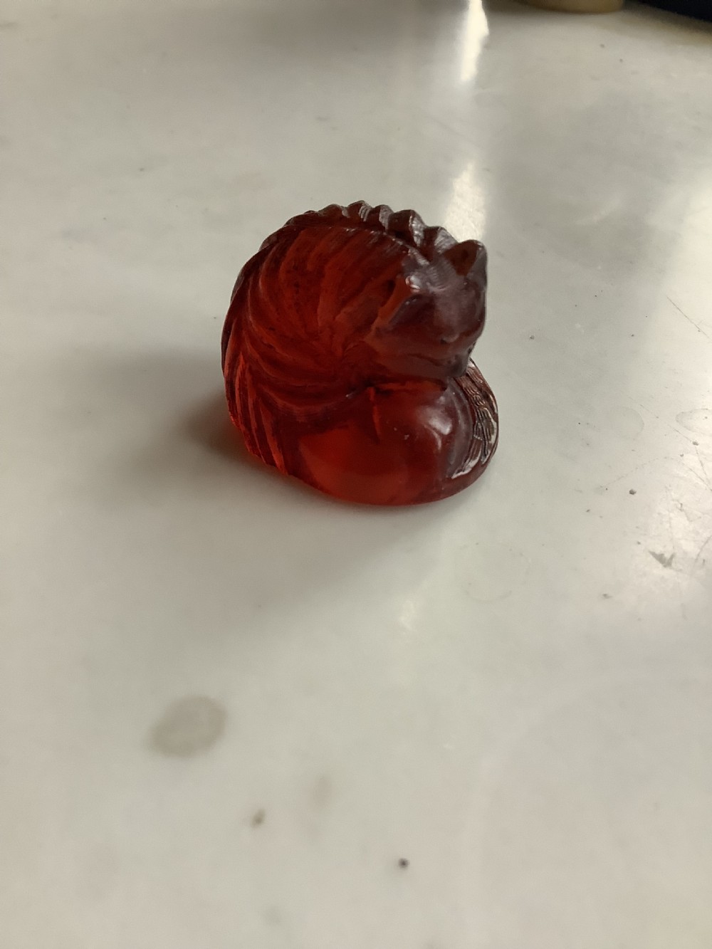 A small, translucent cherry amber carving depicting a curled sleeping cat with incised fur details. View IX