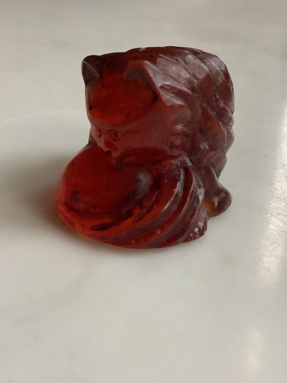 A small, translucent cherry amber carving depicting a curled sleeping cat with incised fur details. View X