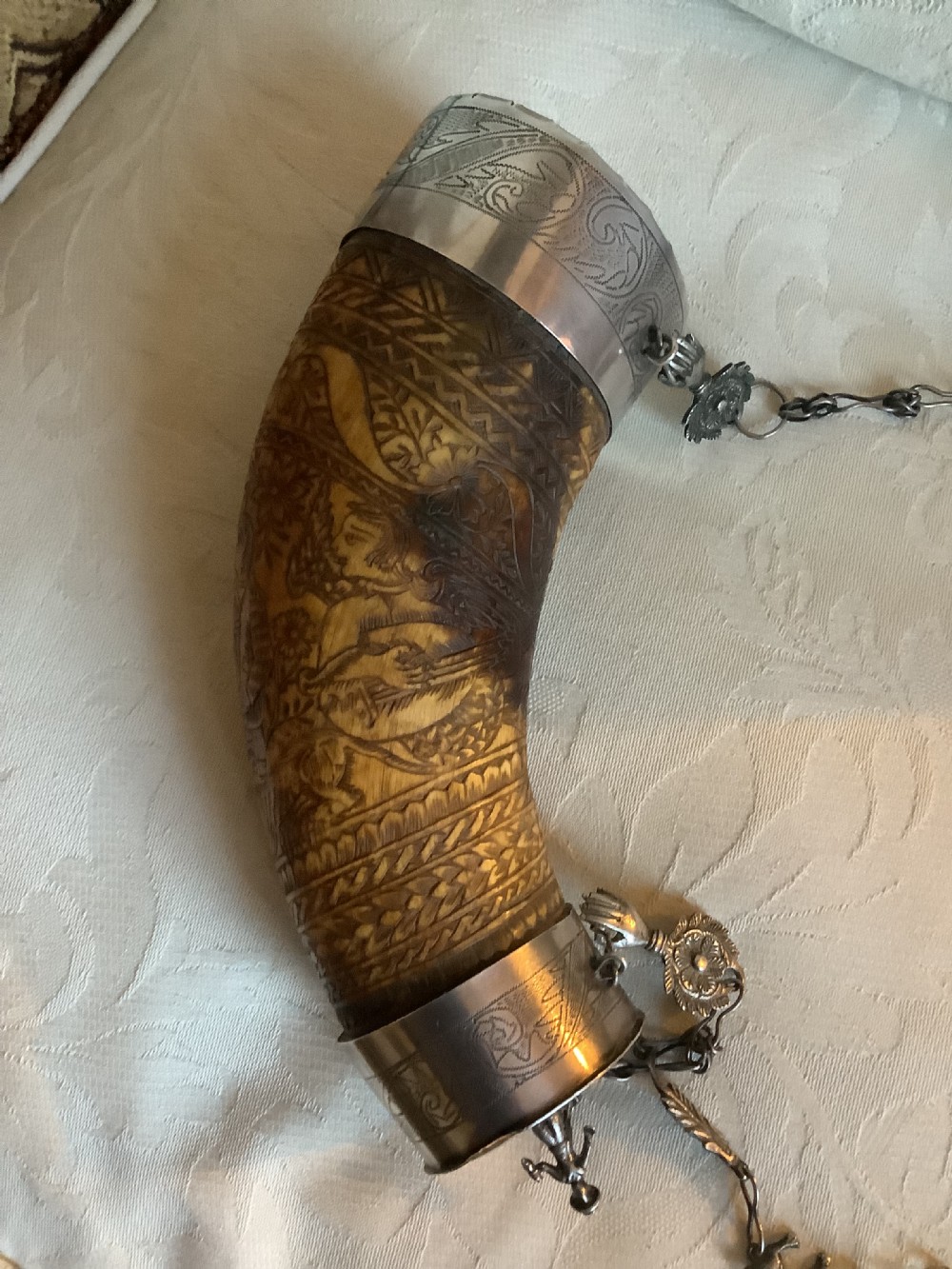 An 18th-century curved horn powder flask featuring intricate surface engravings, silver-coloured metal end caps, and an ornate chain strap. View II