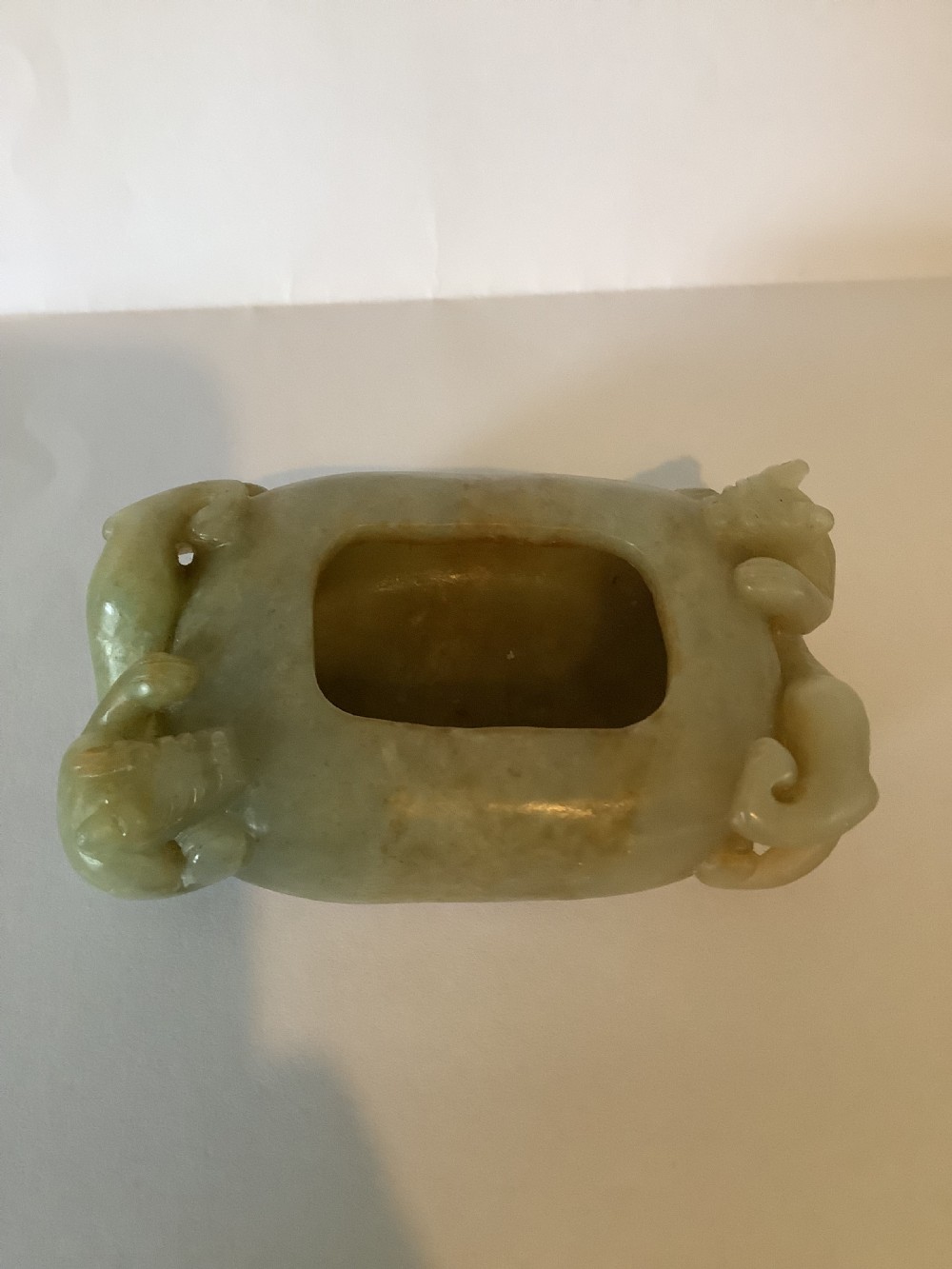 A hollowed pale green jade brush washer featuring high-relief dragon carvings along the outer edges and natural russet undertones.
