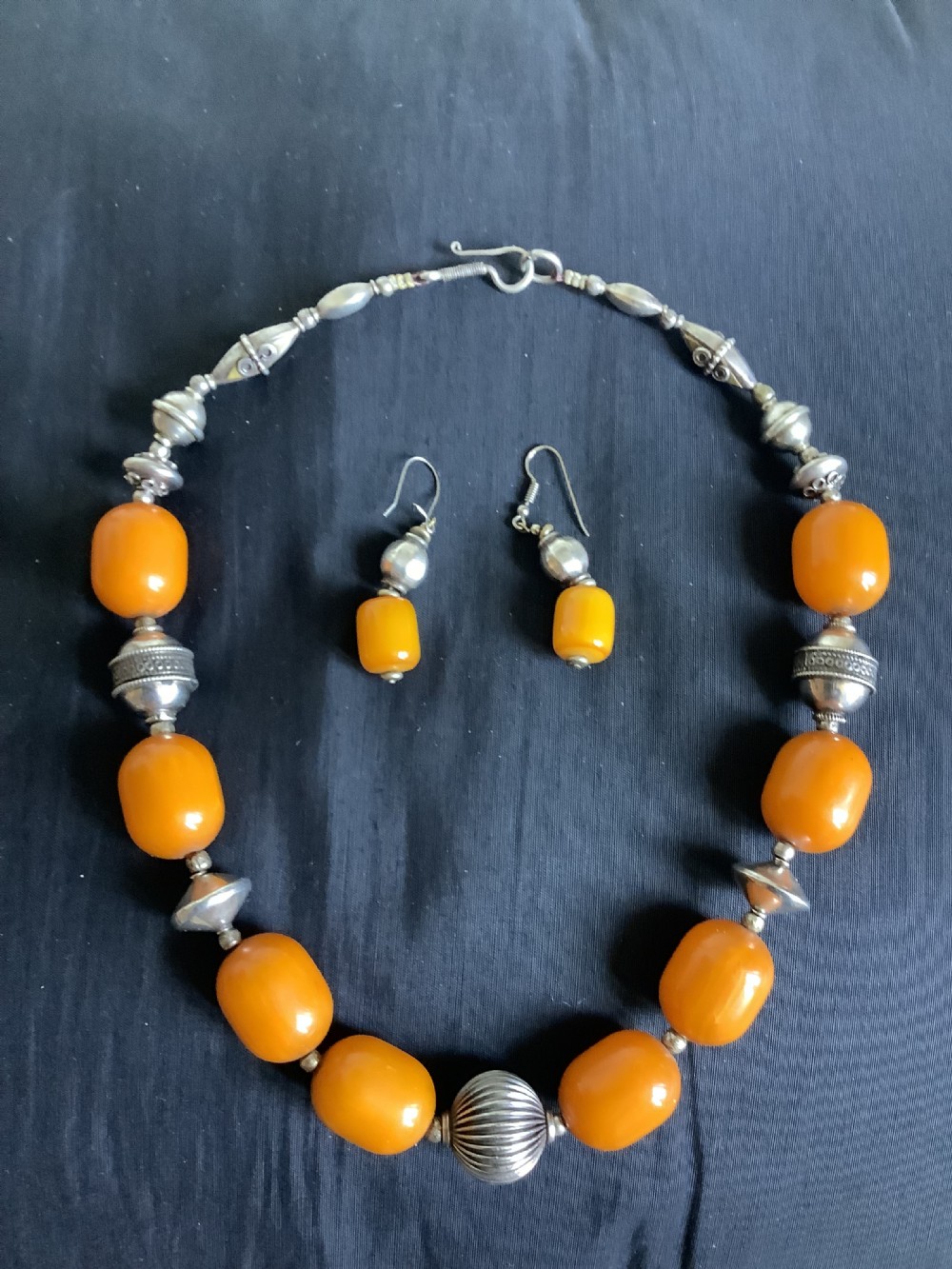 An orange amber bead and sterling silver necklace with matching drop earrings displayed flat on a dark fabric surface.