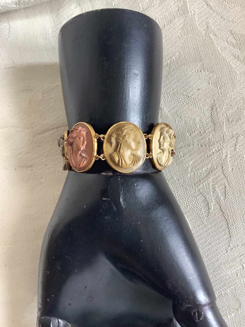A Victorian link bracelet featuring oval lava stone cameos carved with classical profiles in earth tones, set in gilt metal frames.