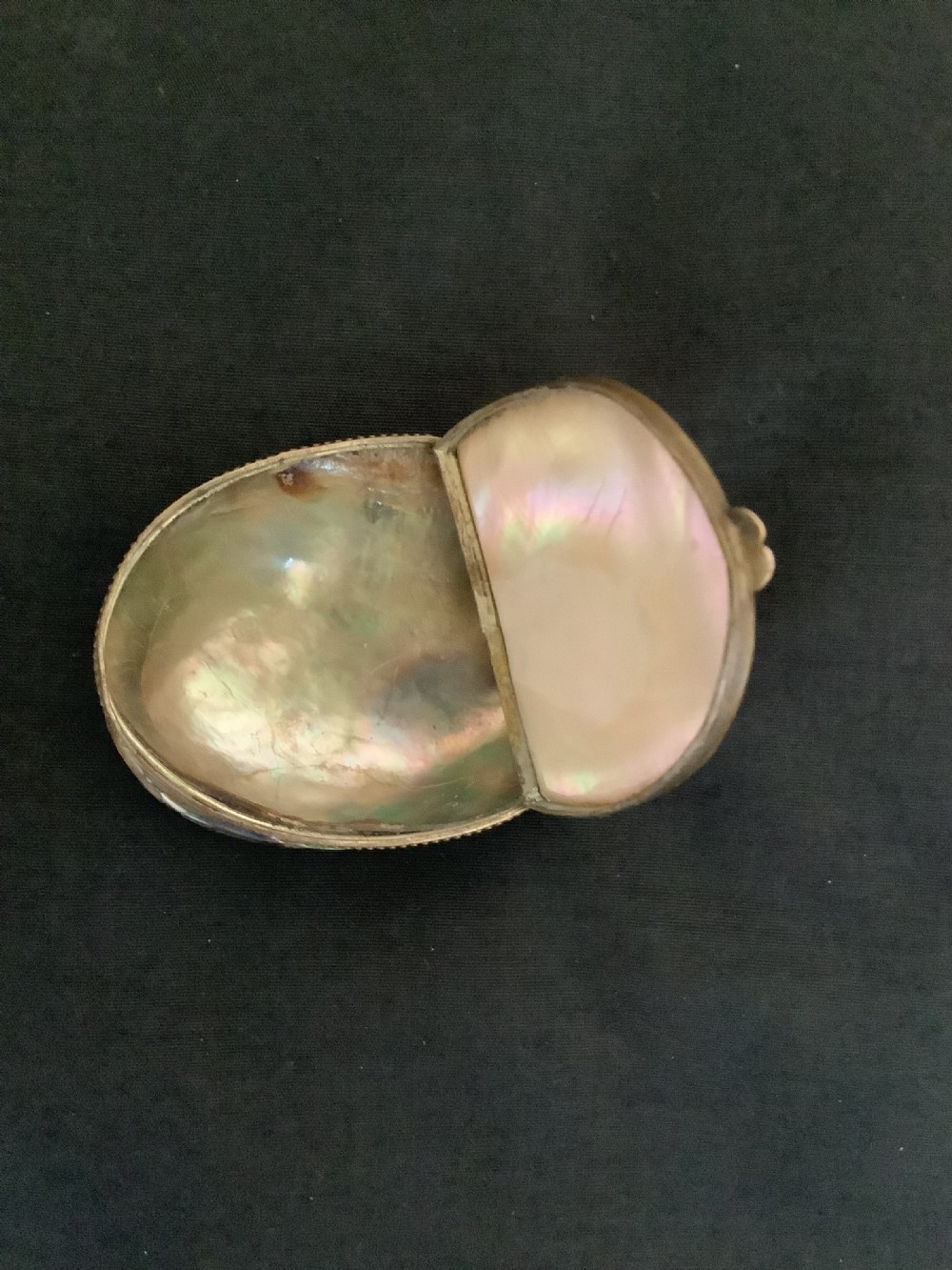 An oval antique snuff box crafted from polished iridescent abalone shell with a metal rim. View II
