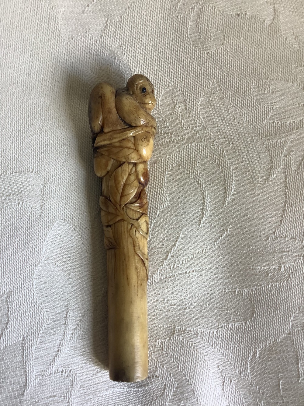 An antique Japanese stag horn parasol handle hand-carved with a monkey figure among leaf and branch motifs.