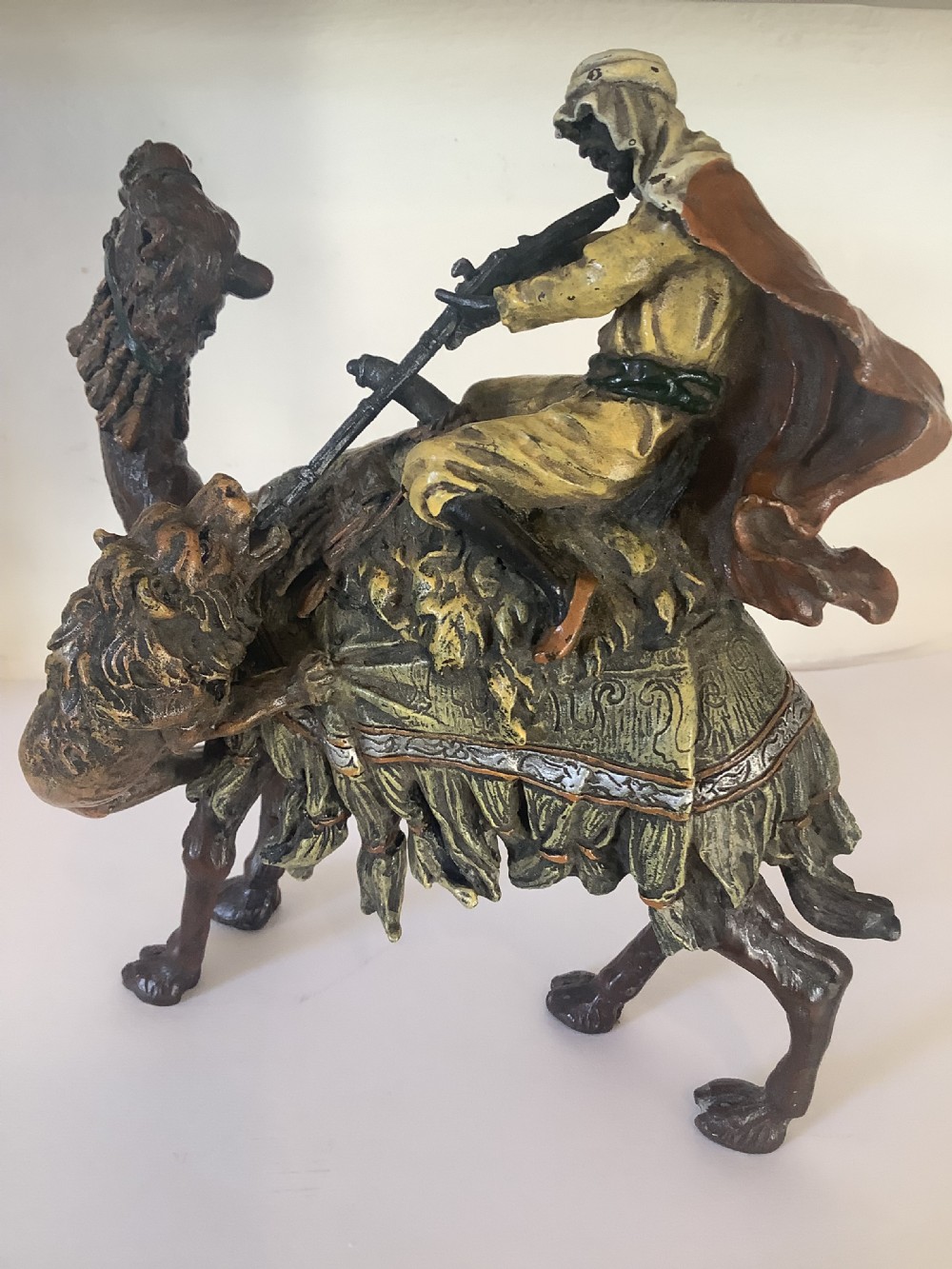 A cold painted bronze sculpture depicting a draped Arabic rider holding a rifle atop a camel.