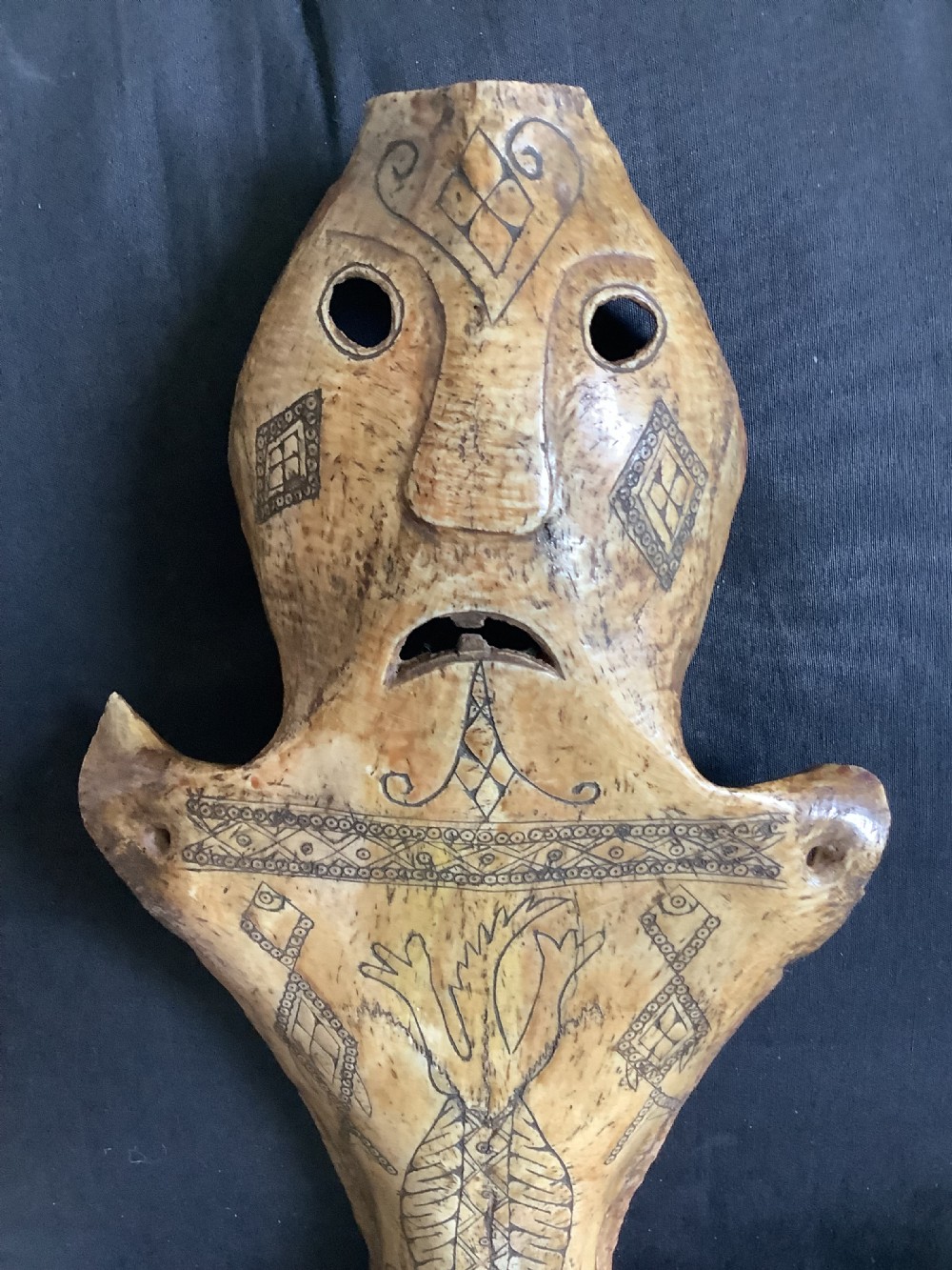 A carved beige animal bone featuring stylised human facial details, incised geometric diamond patterns, and an engraved reptile design. View II