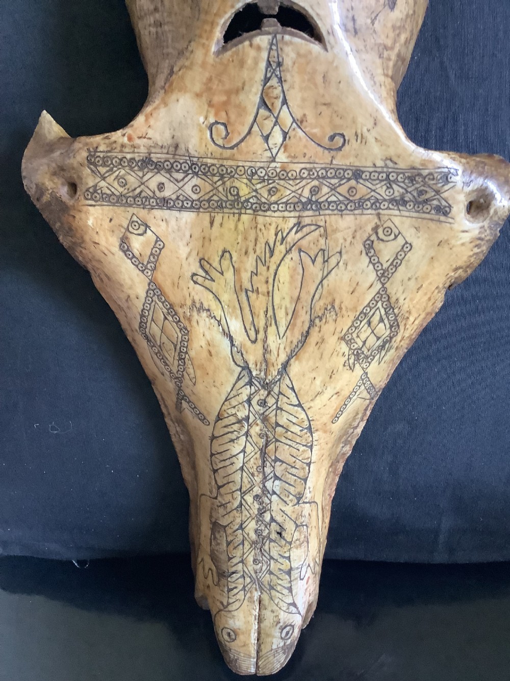 A carved beige animal bone featuring stylised human facial details, incised geometric diamond patterns, and an engraved reptile design. View III