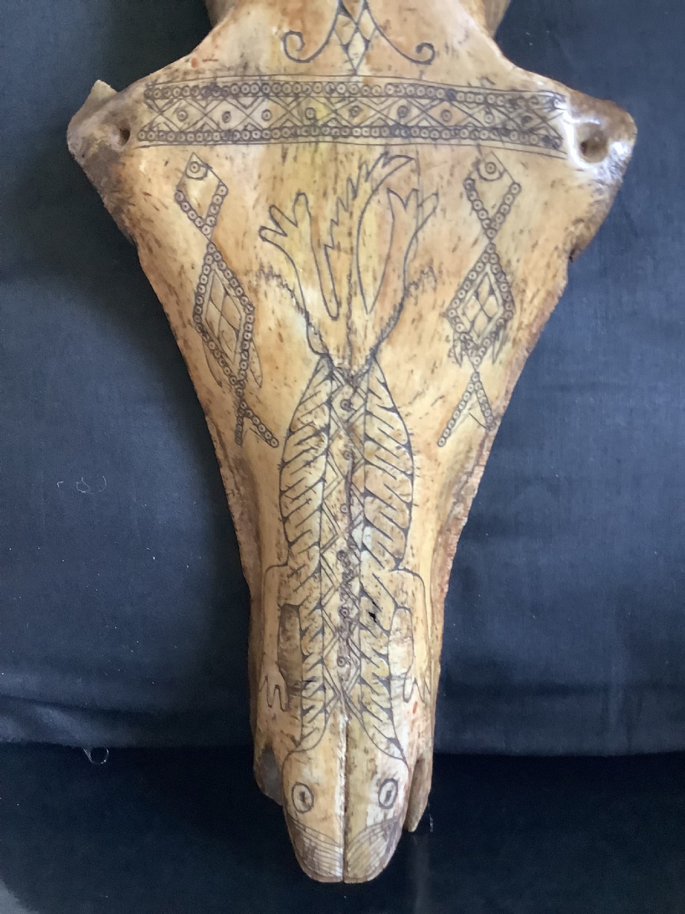 A carved beige animal bone featuring stylised human facial details, incised geometric diamond patterns, and an engraved reptile design. View IV