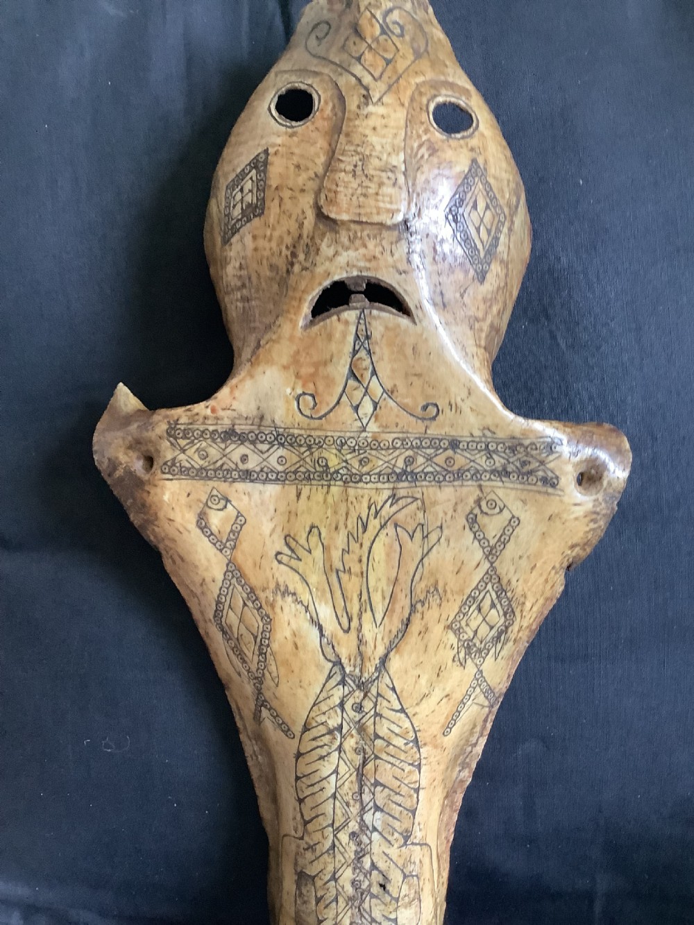 A carved beige animal bone featuring stylised human facial details, incised geometric diamond patterns, and an engraved reptile design. View VI