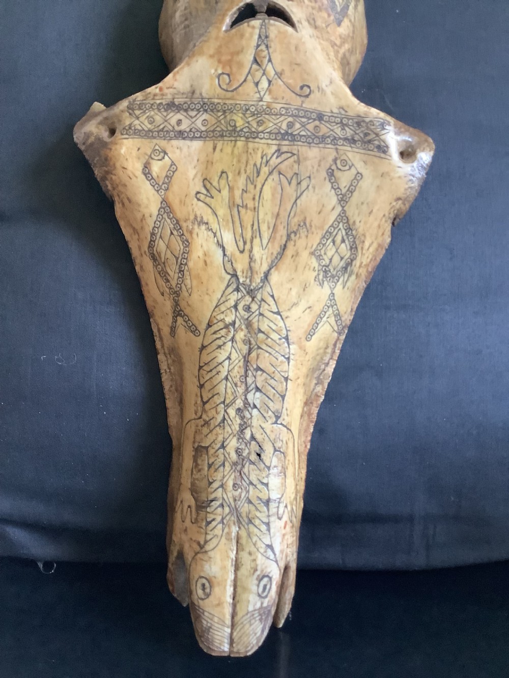 A carved beige animal bone featuring stylised human facial details, incised geometric diamond patterns, and an engraved reptile design. View VII