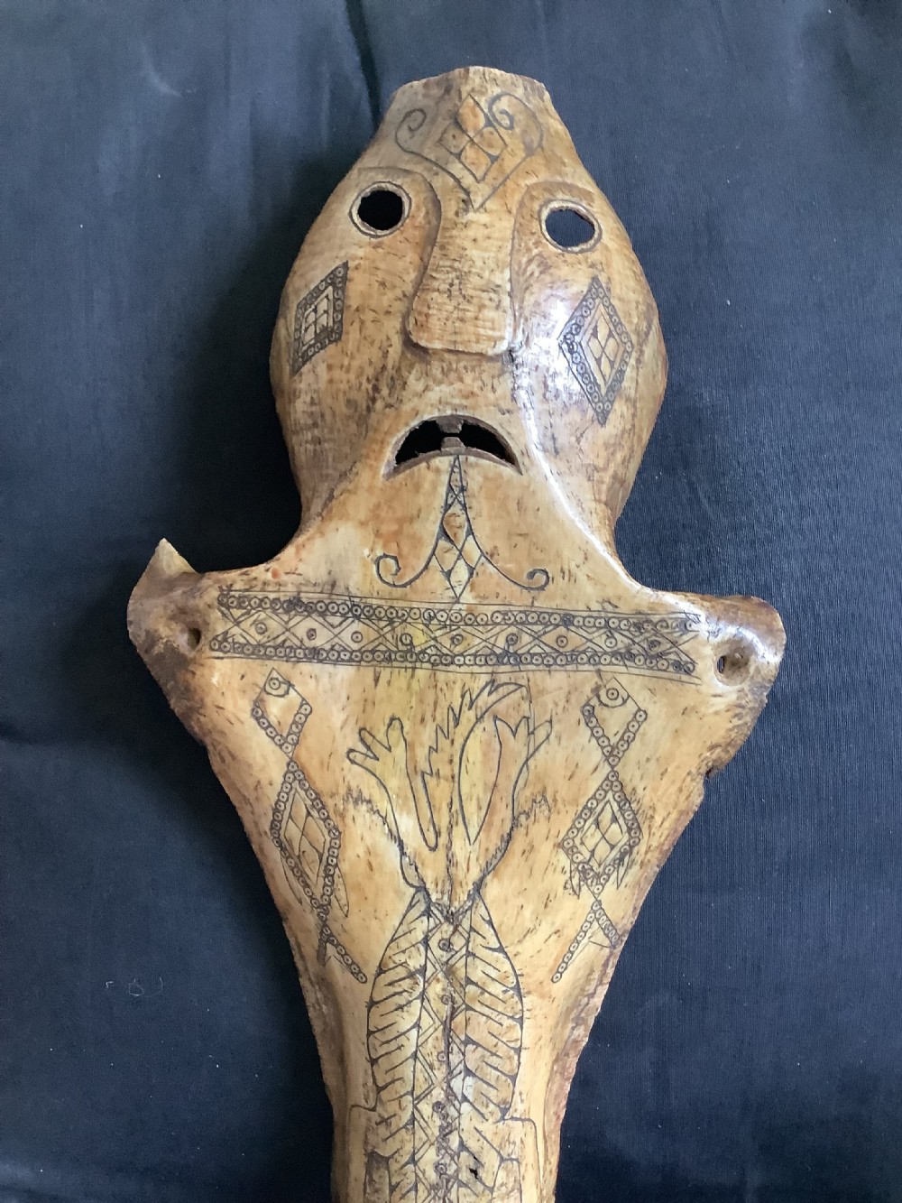 A carved beige animal bone featuring stylised human facial details, incised geometric diamond patterns, and an engraved reptile design. View VIII