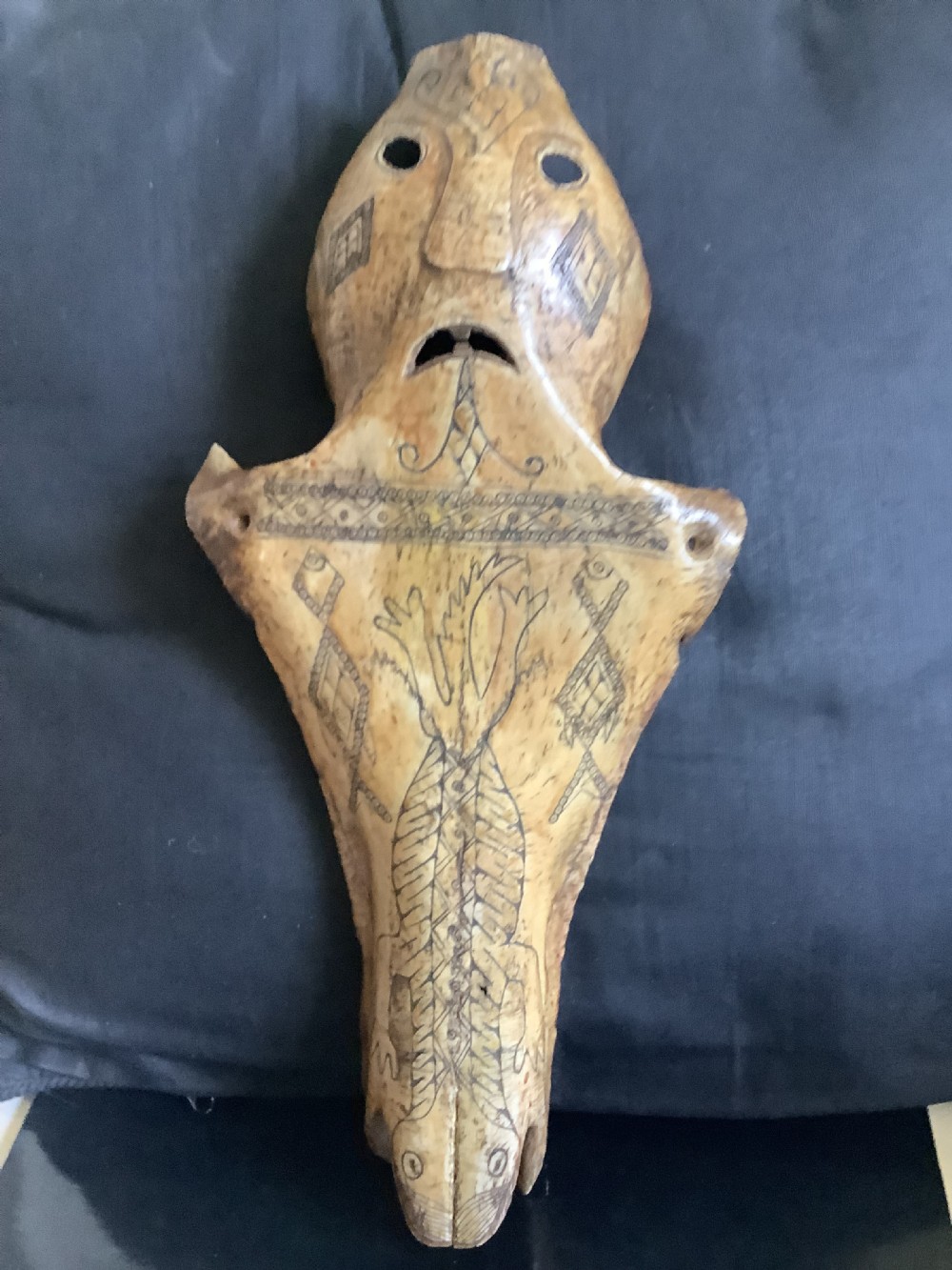 A carved beige animal bone featuring stylised human facial details, incised geometric diamond patterns, and an engraved reptile design. View IX