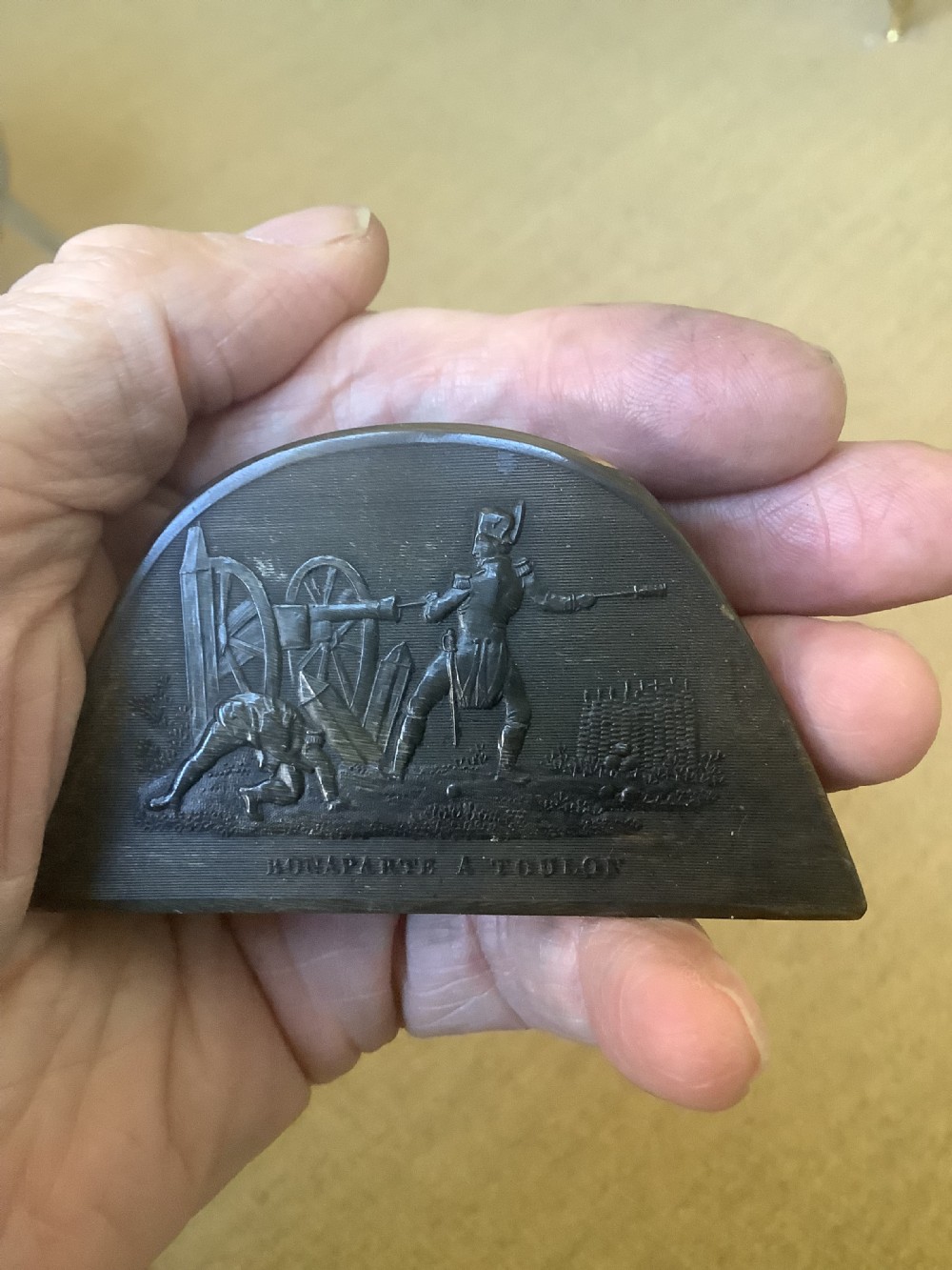A dark brown pressed horn snuff box shaped like a bicorn hat with a relief scene depicting Napoleon at Toulon.
