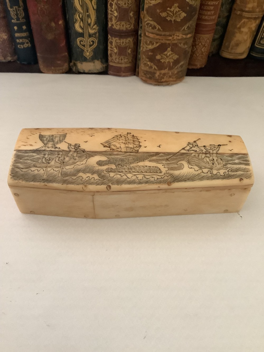 A cream-coloured bone coffin box featuring etched scrimshaw depictions of a whaling scene, boats, and ocean waves on the lid.