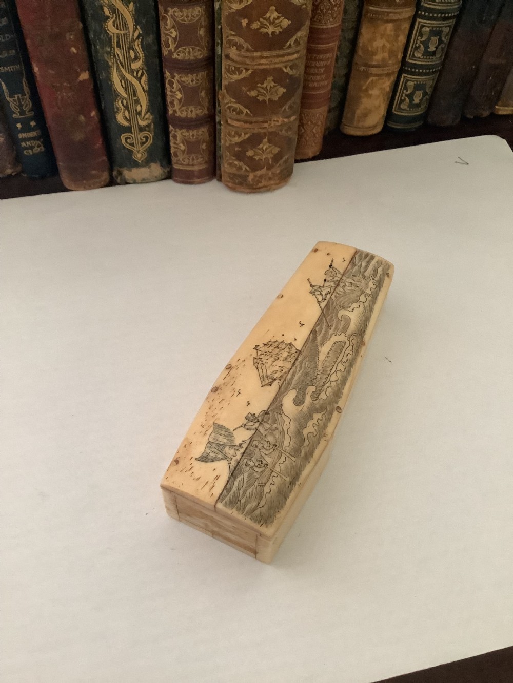 A cream-coloured bone coffin box featuring etched scrimshaw depictions of a whaling scene, boats, and ocean waves on the lid. View VI