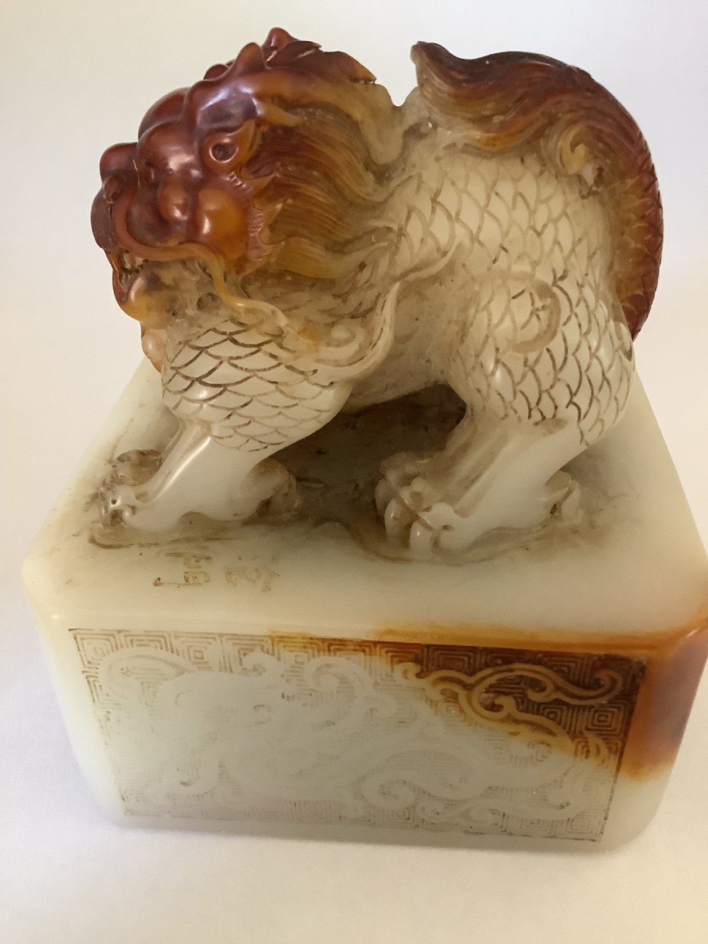 A carved cream and russet jade-style Chinese desk seal featuring a detailed guardian lion finial atop a square base.