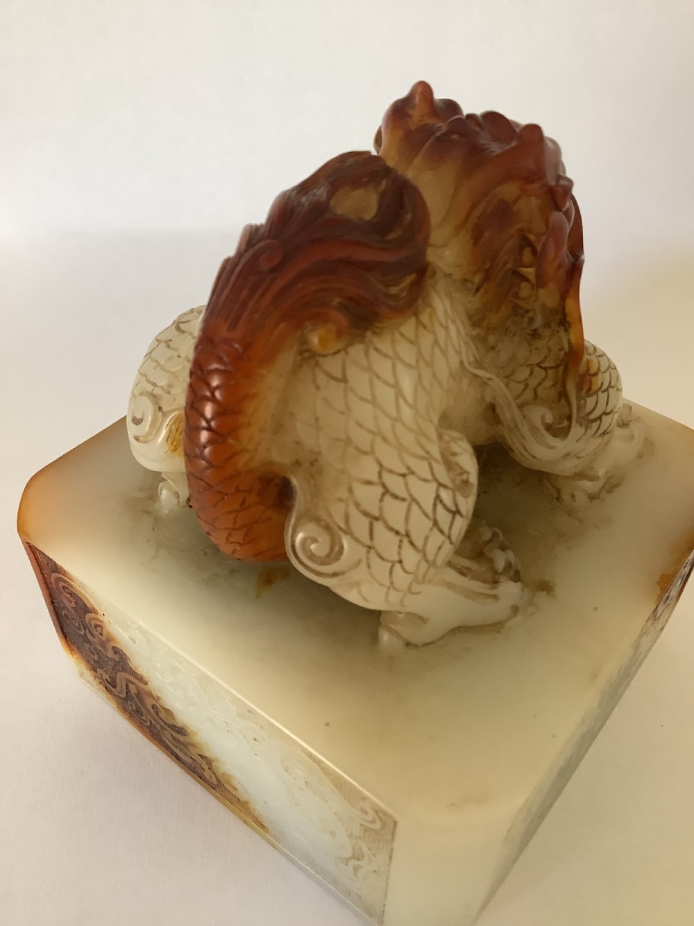 A carved cream and russet jade-style Chinese desk seal featuring a detailed guardian lion finial atop a square base. View X