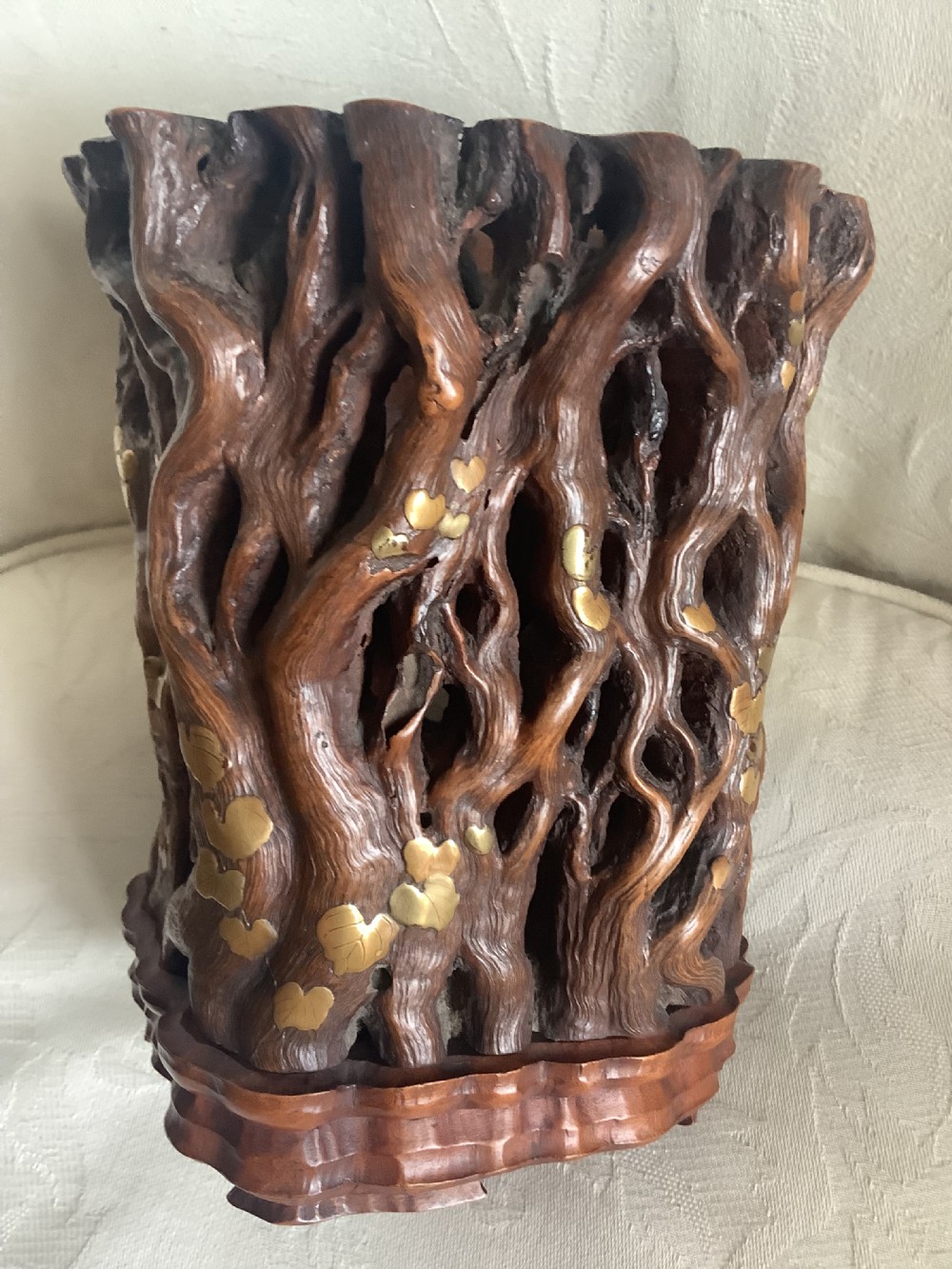 A cylindrical Chinese carved hardwood brush pot featuring openwork gnarled vine motifs inlaid with brass leaves, resting on a fitted carved wooden base. View VIII