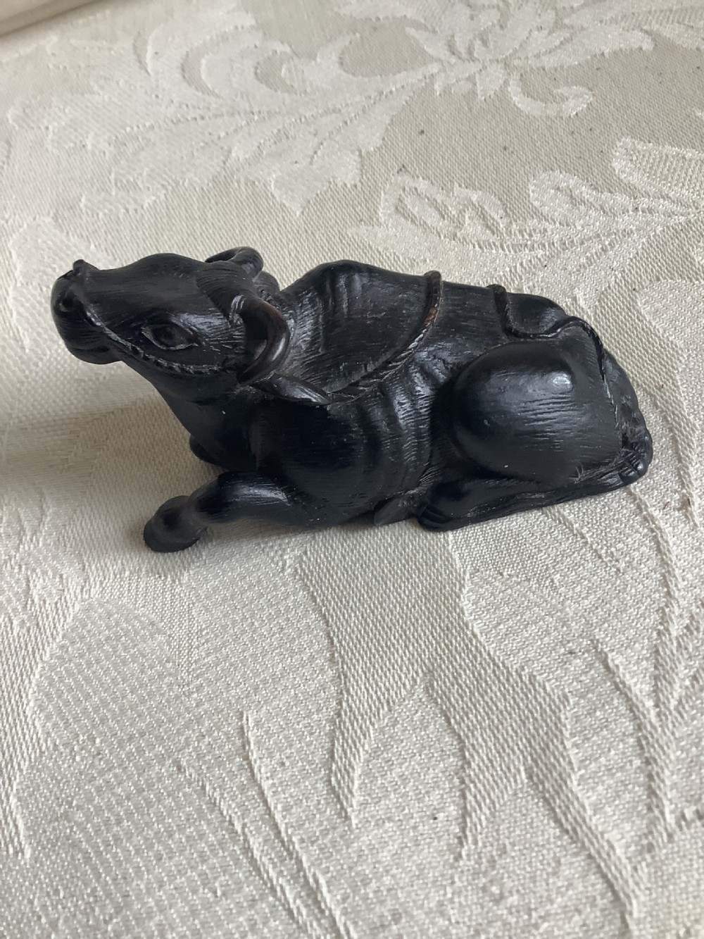 A dark carved wooden Japanese netsuke depicting a recumbent water buffalo with curved horns and hair detail. View II