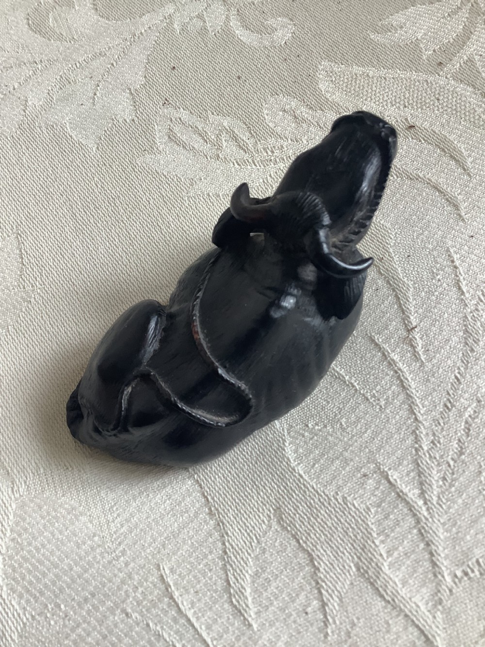 A dark carved wooden Japanese netsuke depicting a recumbent water buffalo with curved horns and hair detail. View III