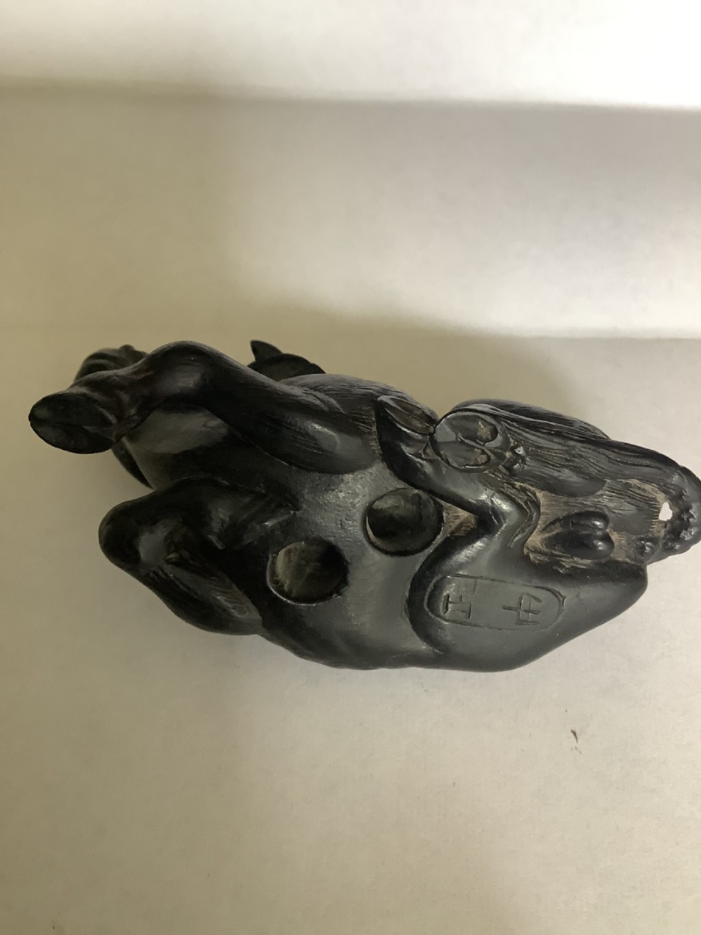 A dark carved wooden Japanese netsuke depicting a recumbent water buffalo with curved horns and hair detail. View V