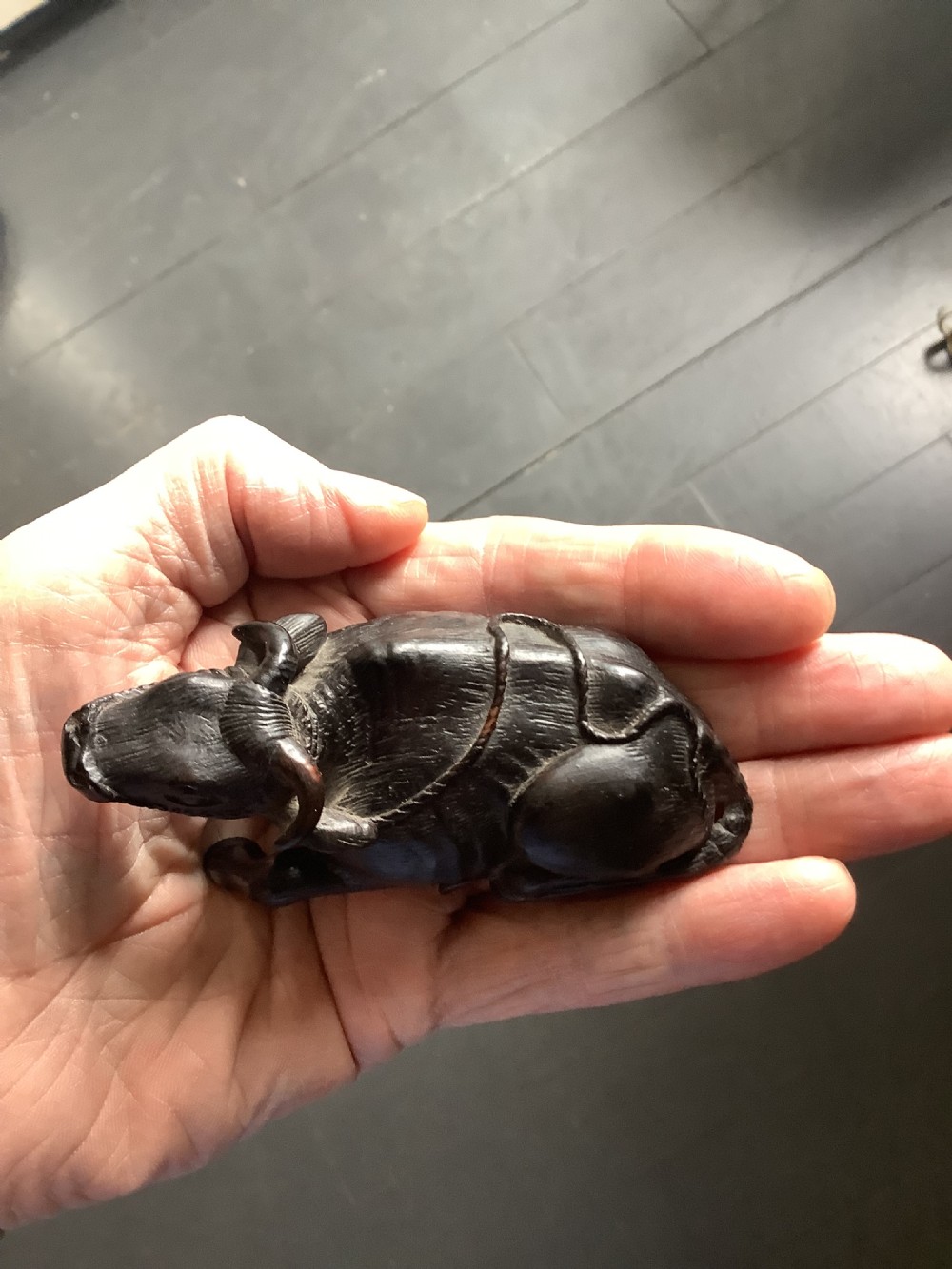 A dark carved wooden Japanese netsuke depicting a recumbent water buffalo with curved horns and hair detail. View VI