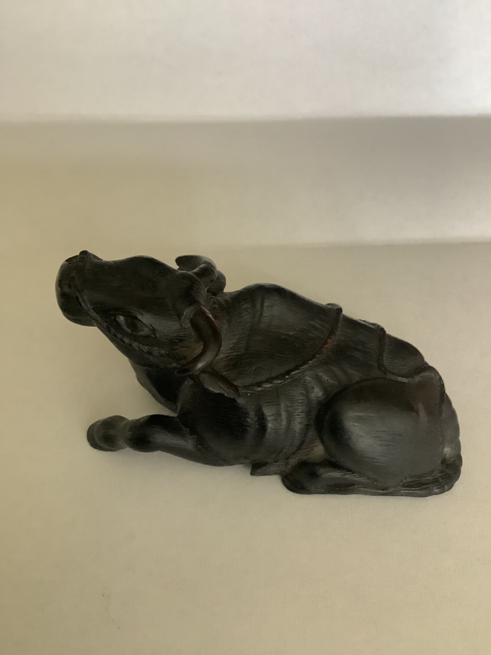 A dark carved wooden Japanese netsuke depicting a recumbent water buffalo with curved horns and hair detail.