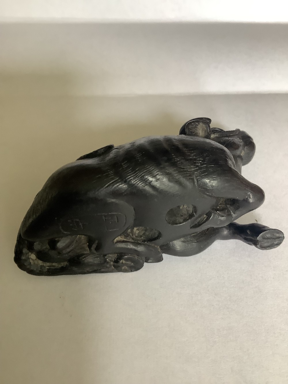 A dark carved wooden Japanese netsuke depicting a recumbent water buffalo with curved horns and hair detail. View VIII