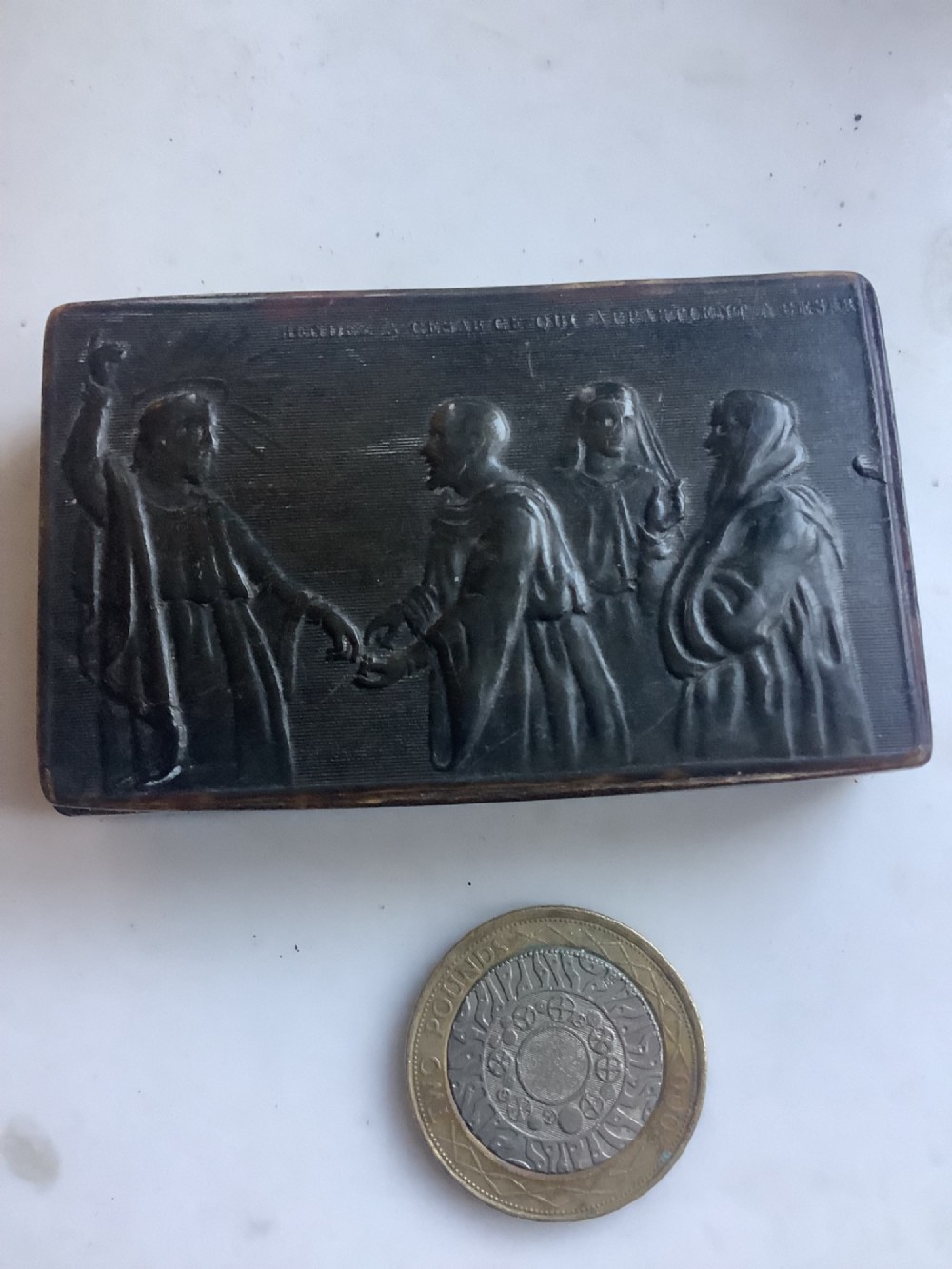 A rectangular dark brown pressed horn snuff box displaying a moulded relief of a biblical scene with figures and a French inscription on the top lid.