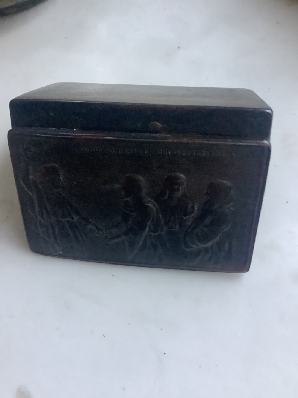 A rectangular dark brown pressed horn snuff box displaying a moulded relief of a biblical scene with figures and a French inscription on the top lid. View V