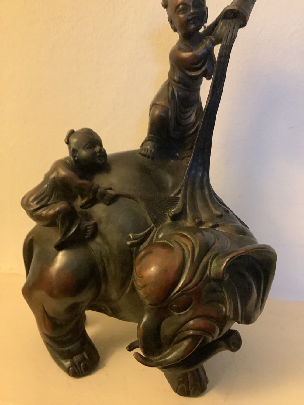 A dark brown patinated bronze sculpture depicting an elephant with two young boys on its back. View IV