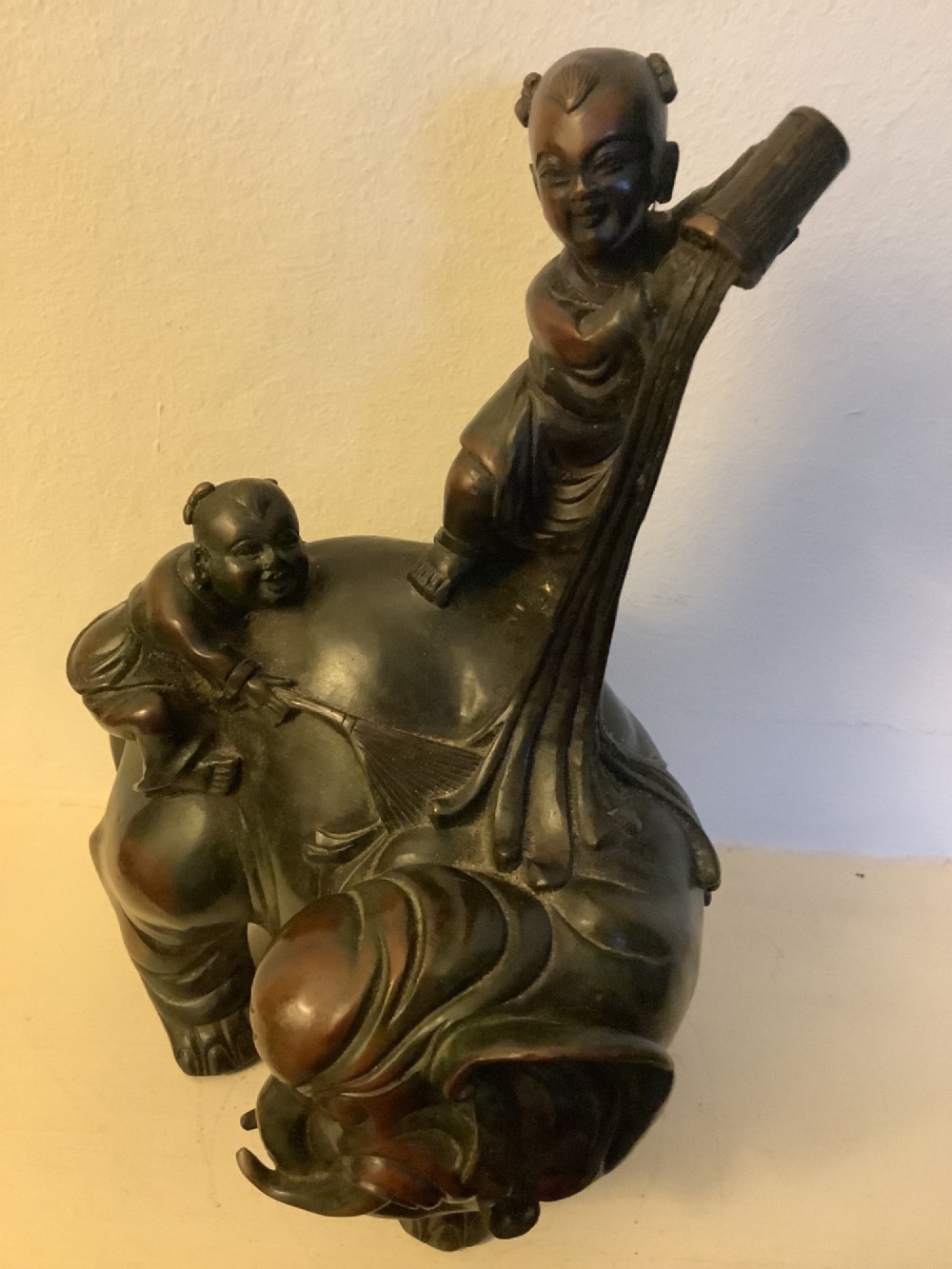 A dark brown patinated bronze sculpture depicting an elephant with two young boys on its back. View VII