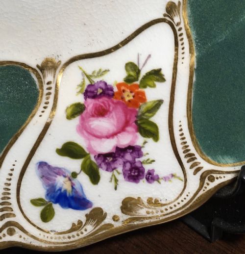 fig 2. A circular Regency period Bloor Derby porcelain dessert plate featuring deep green rim panels, hand-painted floral bouquets, and gilded scrolling borders surrounding a central botanical motif.