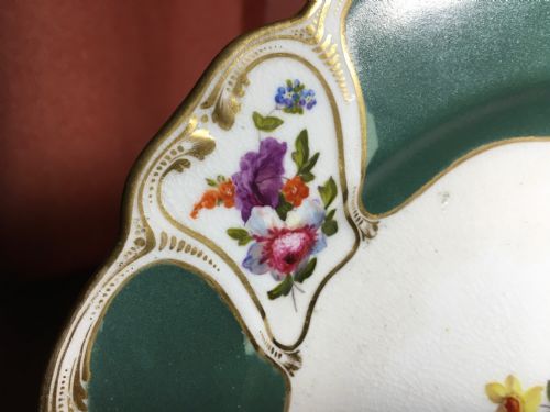 fig 3. A circular Regency period Bloor Derby porcelain dessert plate featuring deep green rim panels, hand-painted floral bouquets, and gilded scrolling borders surrounding a central botanical motif.