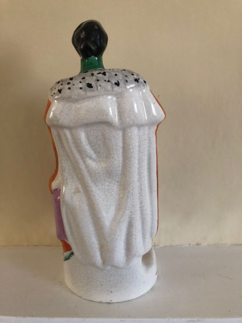 fig 1. A Victorian Staffordshire earthenware figure depicting Prince Albert standing in a green tunic and orange cloak on a rounded pedestal base.