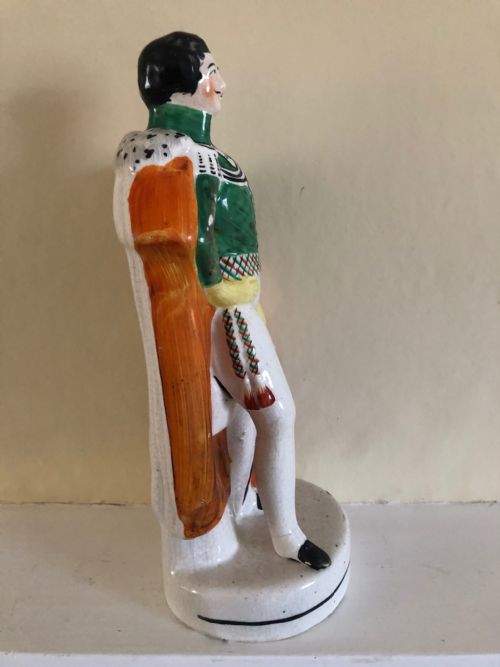 fig 2. A Victorian Staffordshire earthenware figure depicting Prince Albert standing in a green tunic and orange cloak on a rounded pedestal base.